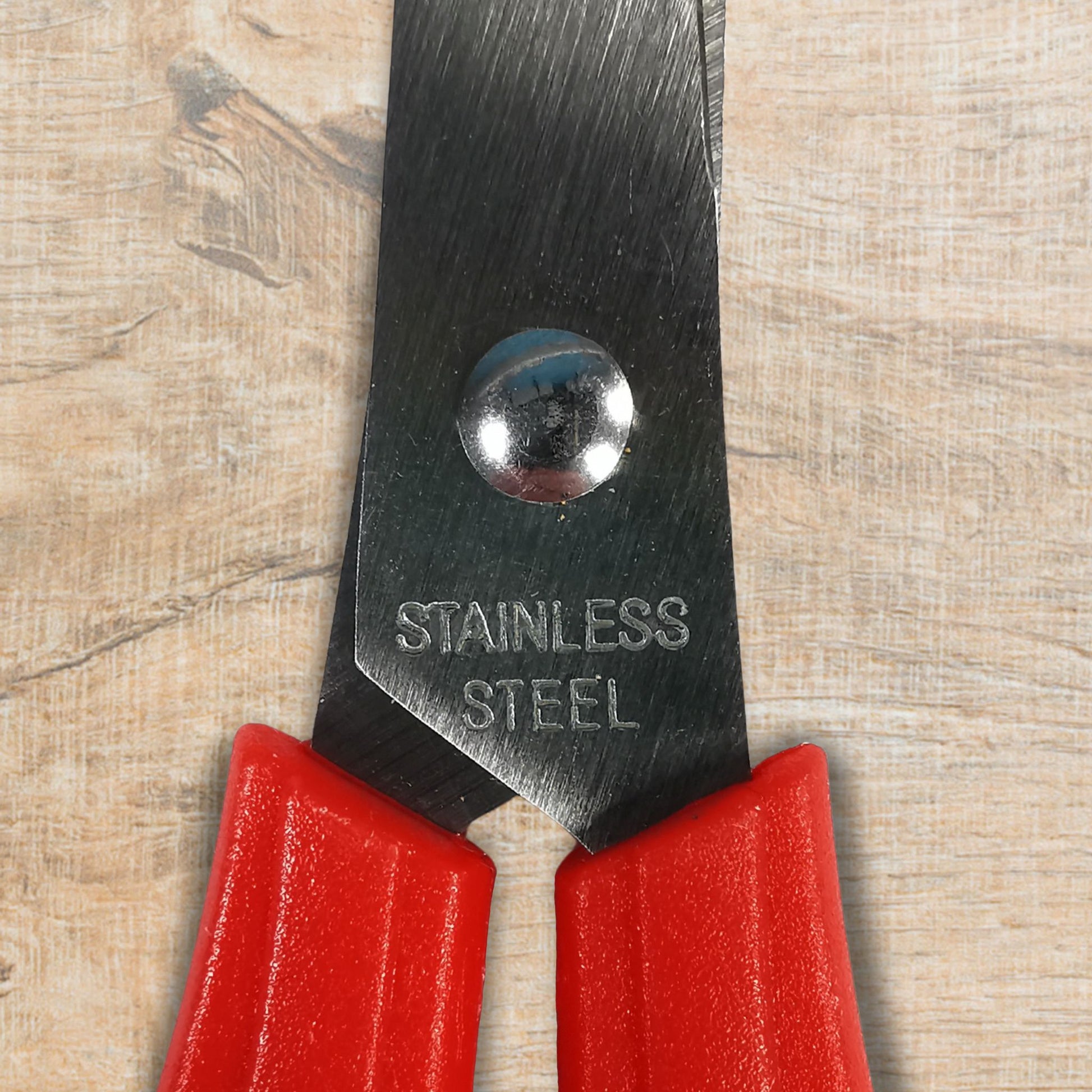 Red-handled pliers with a 'Stainless Steel' label on a wooden surface