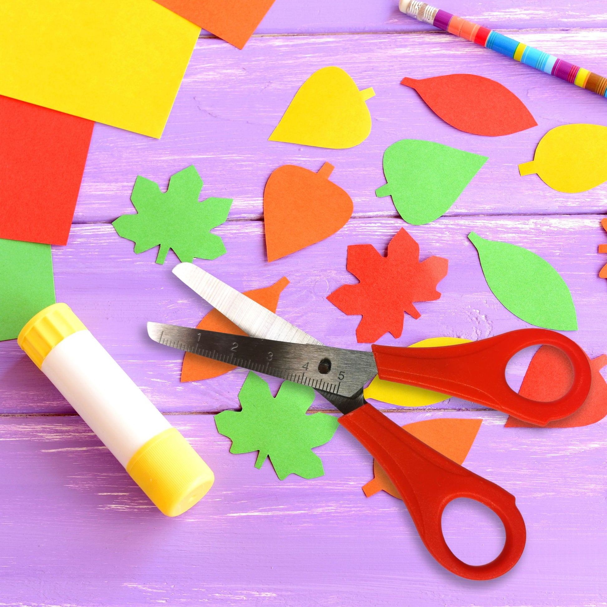 Colorful paper leaves, scissors, and glue on a purple wooden surface