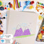 Children's drawing of mountains with colored pencils and art supplies around on white sugar paper