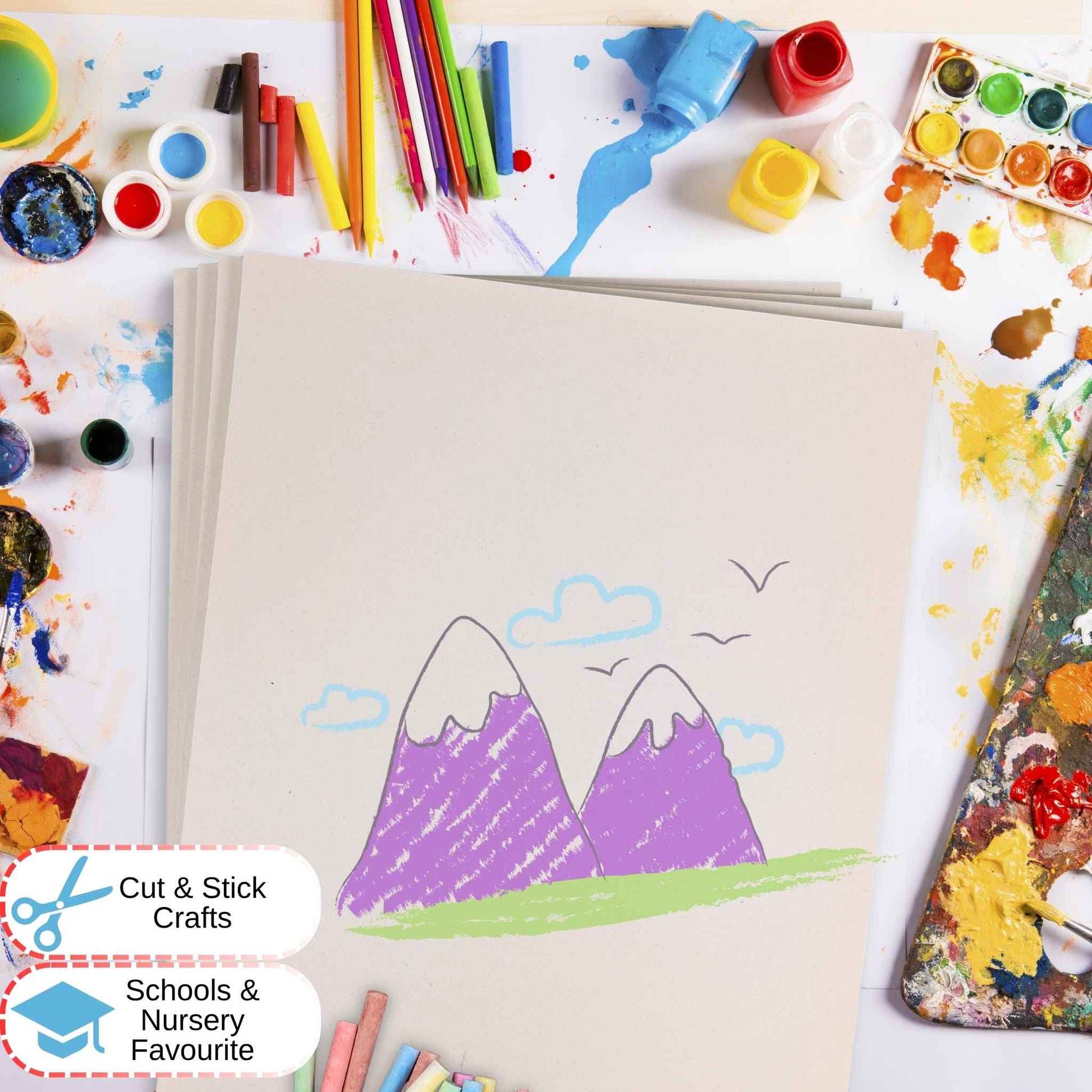 Children's drawing of mountains with colored pencils and art supplies around on white sugar paper