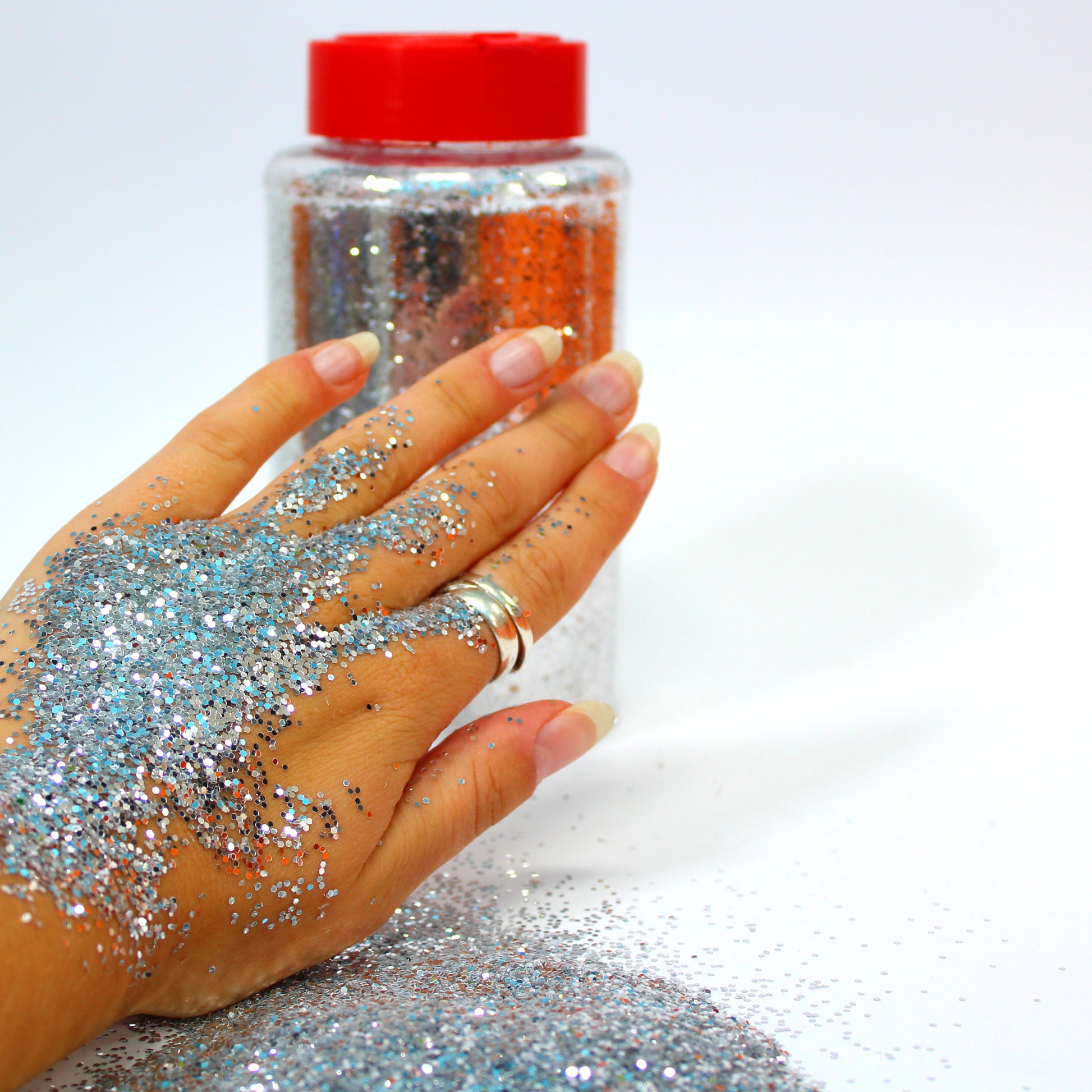 Hand with glittery powder and a jar of glitter on a white background