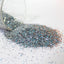 silver Glitter spilling from a clear container on a white surface