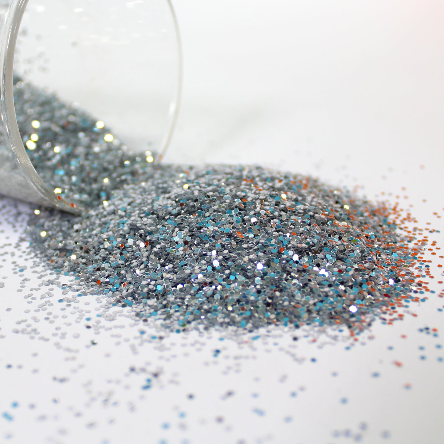 silver Glitter spilling from a clear container on a white surface